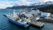Barco pesquero amarrado en un muelle industrial de Ushuaia, con instalaciones portuarias y montañas nevadas al fondo.