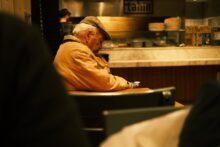 Hombre anciano con un teléfono móvil en sus manos sentado en una cafetería