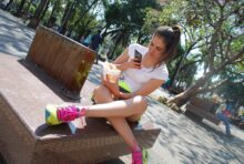 Joven usando su celular mientras come helado en un espacio público al aire libre