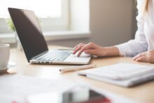 Persona trabajando en una laptop sobre un escritorio con cuaderno, bolígrafo y taza de café