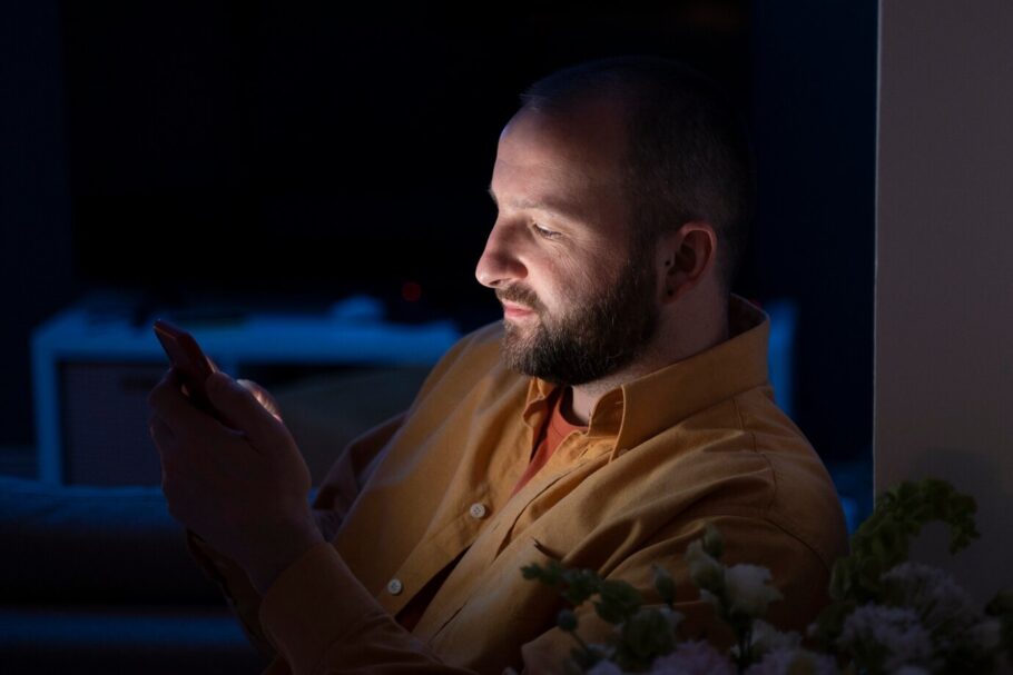 Hombre usando su teléfono móvil de noche, concentrado en la pantalla