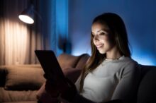 Mujer joven sonriente usando una tablet en el sofá durante la noche