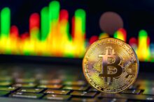 Moneda de Bitcoin sobre teclado con gráfico de velas en segundo plano, representando inversión automatizada en criptomonedas