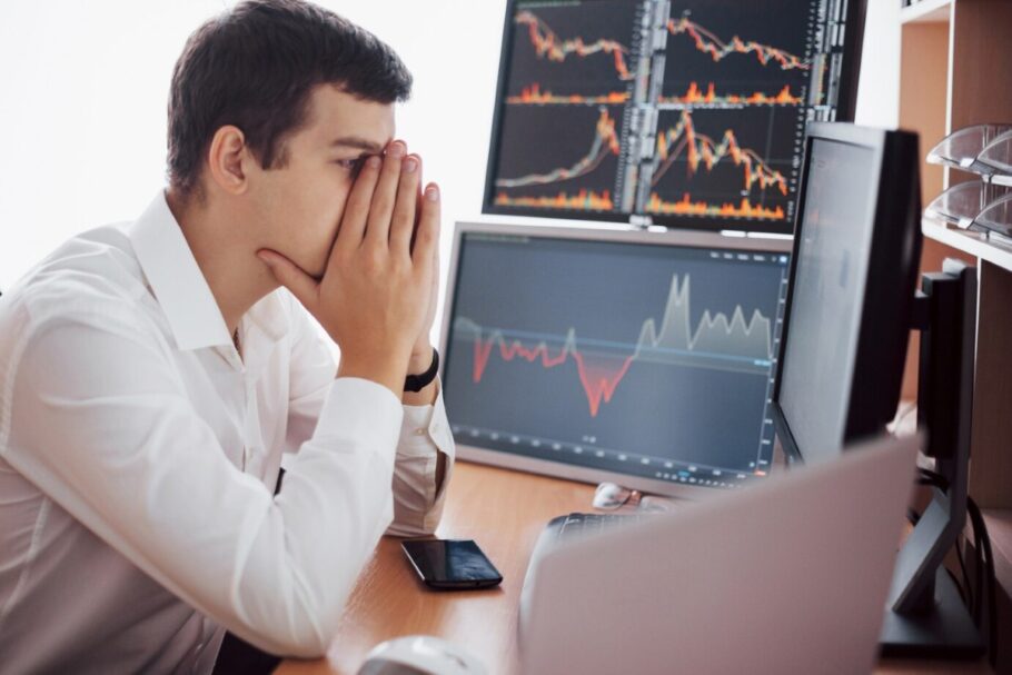 Hombre preocupado mirando gráficos financieros en múltiples pantallas