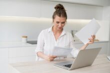 Mujer revisando documentos fiscales frente a una laptop en una cocina moderna