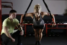 Mujer realizando flexiones con TRX en gimnasio junto a entrenador personal