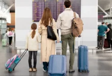 Familia con maletas observando el panel de vuelos en un aeropuerto