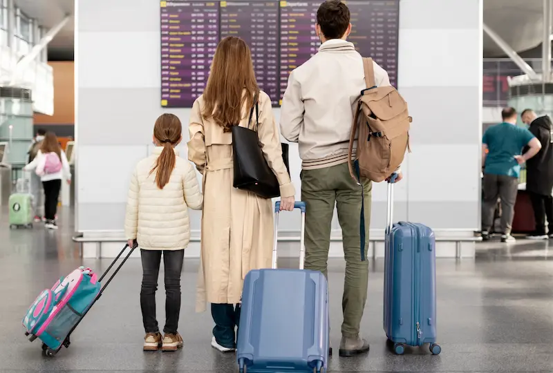 Familia con maletas observando el panel de vuelos en un aeropuerto