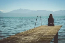 Viajera sentada al final de un muelle de madera sobre un lago con montañas