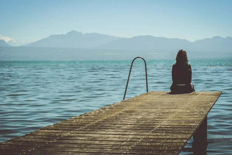 Viajera sentada al final de un muelle de madera sobre un lago con montañas