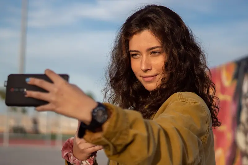 Smiling woman taking a selfie outdoors with iPhone during golden hour