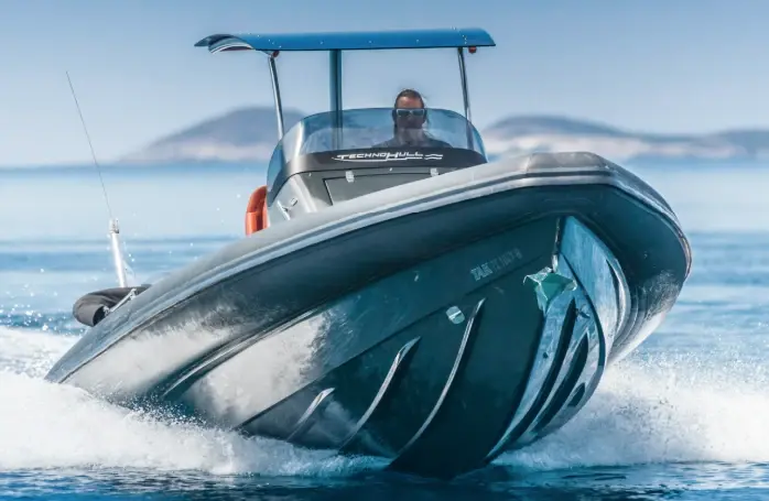 Lancha semirrígida navegando a velocidad en mar calmo, vista frontal del casco en V con T-top y timonel durante una prueba en el agua.