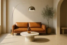 Sala contemporánea con sofá de cuero cognac, mesa redonda de mármol, lámpara de arco en latón y planta de olivo; materiales nobles del diseño italiano.