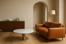 Living minimalista con sofá de cuero cognac, mesa redonda de mármol blanco y aparador de nogal bajo luz natural.