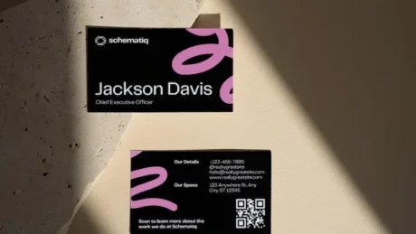 Tarjetas de visita negras con detalles rosas y tipografía blanca sobre una superficie iluminada, ejemplo de diseño moderno y minimalista