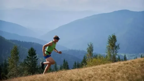 Corredor entrenando en cuestas: running cuesta arriba en una ladera con pasto y montañas al fondo