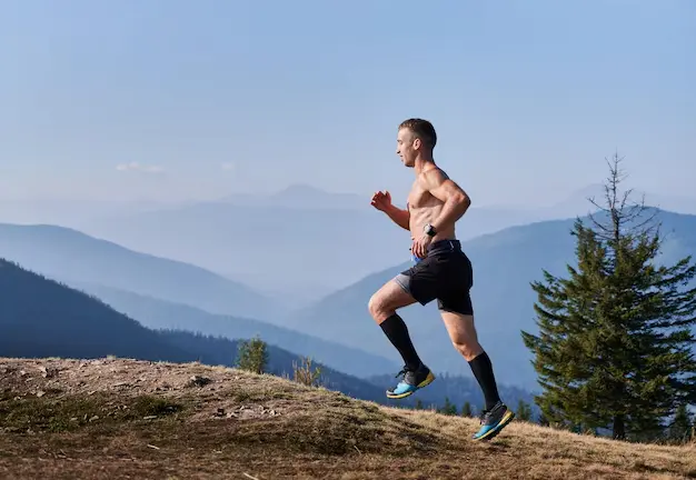 Corredor haciendo sprints en cuesta sobre una loma de montaña, con paisaje de sierras y cielo despejado