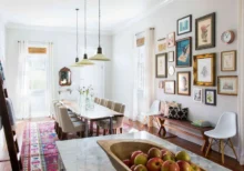 Comedor de concepto abierto con pared galería de cuadros, mesa larga, lámparas colgantes y decoración luminosa en tonos neutros.