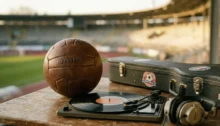 Balón de fútbol de cuero junto a un tocadiscos con vinilo y auriculares en un estadio.