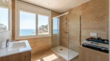 Baño reformado con ducha a ras de suelo, mampara de vidrio y ventana con vista al mar