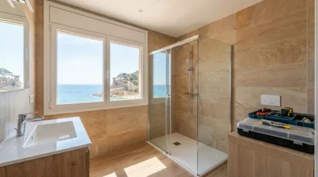 Baño reformado con ducha a ras de suelo, mampara de vidrio y ventana con vista al mar
