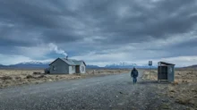 Persona caminando por una ruta de ripio en un paisaje patagónico con montañas al fondo y cielo nublado.