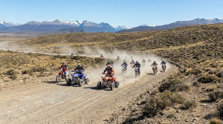 Grupo de motos y cuatriciclos circula por un camino de tierra levantando una nube de polvo en un paisaje de estepa.