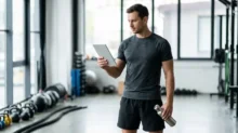Hombre con ropa deportiva mira una tablet en un gimnasio y sostiene una botella de agua