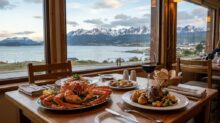 Plato de centolla y copa de vino en una mesa junto a una ventana, con vista al canal y montañas nevadas de Tierra del Fuego.