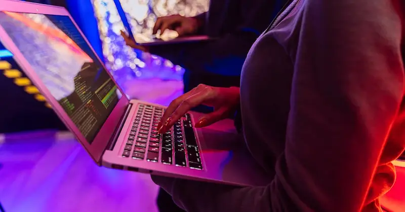 Personas usando laptops con código en pantalla en un ambiente con luces violetas y rojas