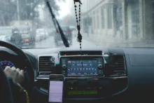 Interior de un auto con la radio encendida y un celular visible frente a un parabrisas con lluvia