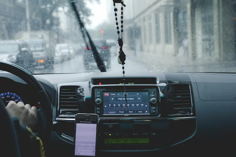 Interior de un auto con la radio encendida y un celular visible frente a un parabrisas con lluvia