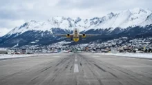 Avión sobre la pista con montañas nevadas y la ciudad al fondo