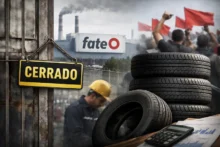 Cartel de CERRADO, neumáticos apilados y planta de FATE con manifestantes al fondo