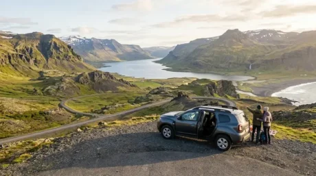 Coche estacionado frente a un valle con montañas, lago y camino panorámico