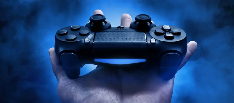 Una mano sostiene un control de videojuegos oscuro frente a un fondo azul