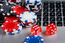 Fichas de poker rojas, azules y negras sobre un teclado, junto a dos dados rojos iluminados
