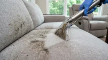 Extraction tool cleaning visible dirt from a light fabric sofa during professional upholstery cleaning