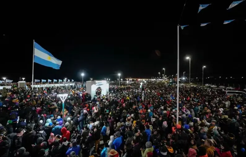 Multitud reunida de noche junto a una bandera argentina durante la vigilia de Malvinas