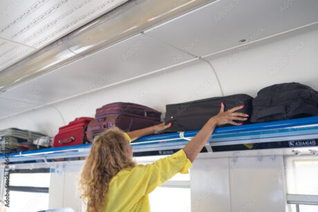 Businesswoman taking bag from luggage compartment in train. Hands take off hand luggage.
