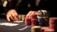 Fichas de póker apiladas sobre una mesa de casino con cartas y manos desenfocadas al fondo