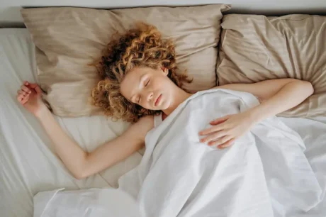 Mujer dormida en una cama con sábanas blancas y almohadas beige