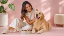 Mujer acaricia a un golden retriever junto a un bowl con alimento seco en un ambiente pastel