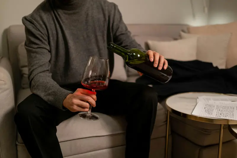 Persona sirviendo vino en una copa mientras está sentada junto a una cama