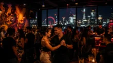 Pareja bailando salsa en un club con barra iluminada, público y skyline nocturno de Londres