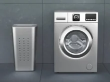 Lavarropas automático de carga frontal junto a un cesto de ropa en un lavadero gris.