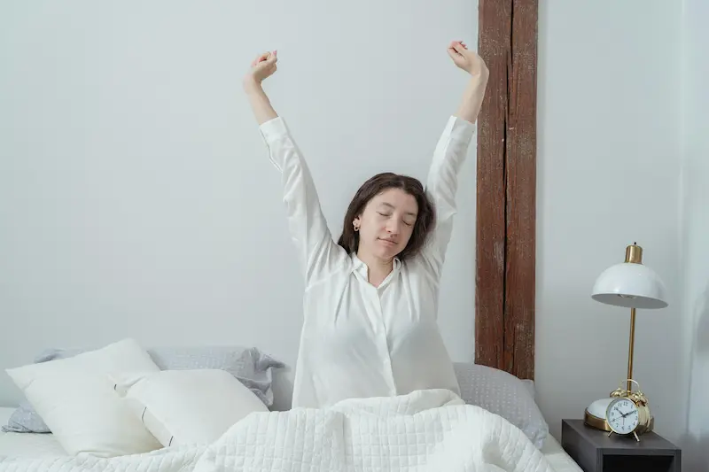 Mujer sentada en la cama se estira con los brazos levantados al despertar