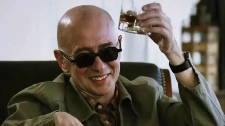 Indio Solari con anteojos oscuros sonríe mientras levanta un vaso en una escena interior
