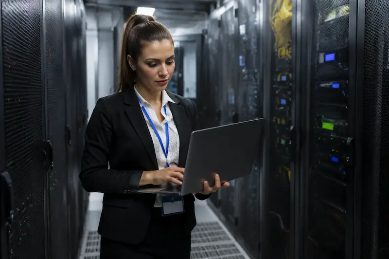 Profesional con notebook entre racks de servidores en un centro de datos
