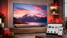 Televisor en un living moderno junto a una laptop, un celular y bolsas de compra online
